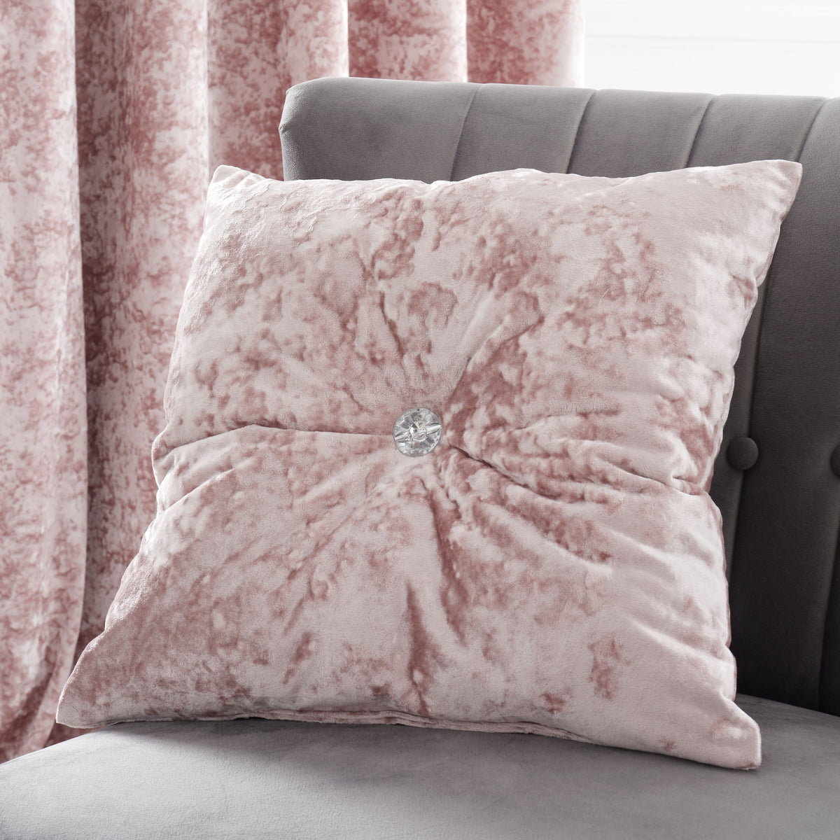 Pink textured pillow with a central gemstone on a gray sofa, with pink curtains in the background.