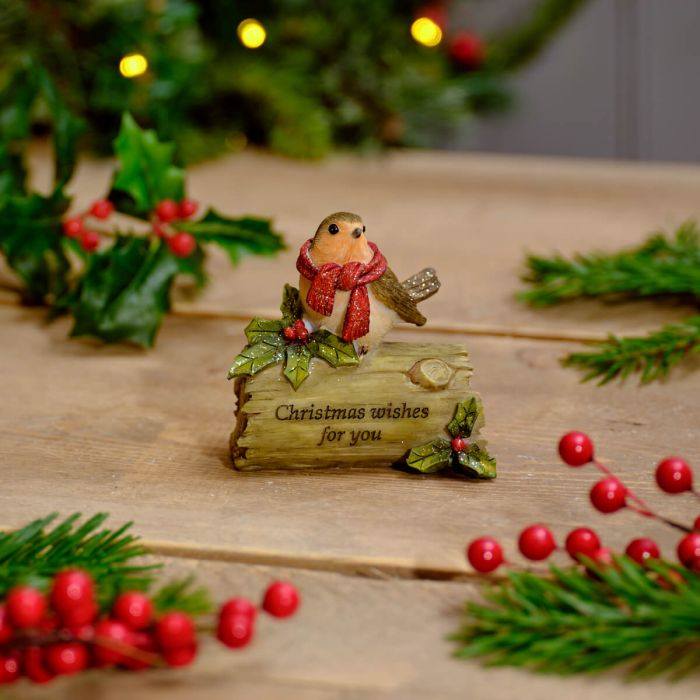Decorative Christmas figurine with a bird wearing a scarf on a wooden surface with holly and berries.