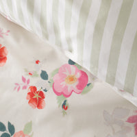 Close-up of a bedding set showing a cream-colored duvet cover with a pink, red, and green floral print, layered over a matching pillowcase with vertical sage green and white stripes.