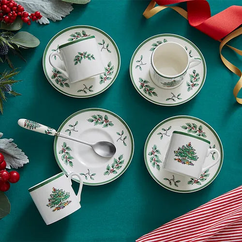 Set of Christmas-themed ceramic mugs and saucers on a green surface with decorative elements.